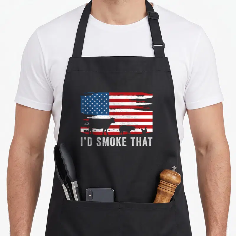 Vintage smoke barbecue apron - Distressed US flag with cow pig chicken silhouettes and I'D SMOKE THAT text — shown on a black cotton canvas apron against a white background