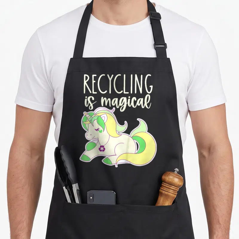 Toddler unicorn apron - Cartoon unicorn with yellow mane wearing purple recycle symbol pendant below stacked text — shown on a black cotton canvas apron against a white background