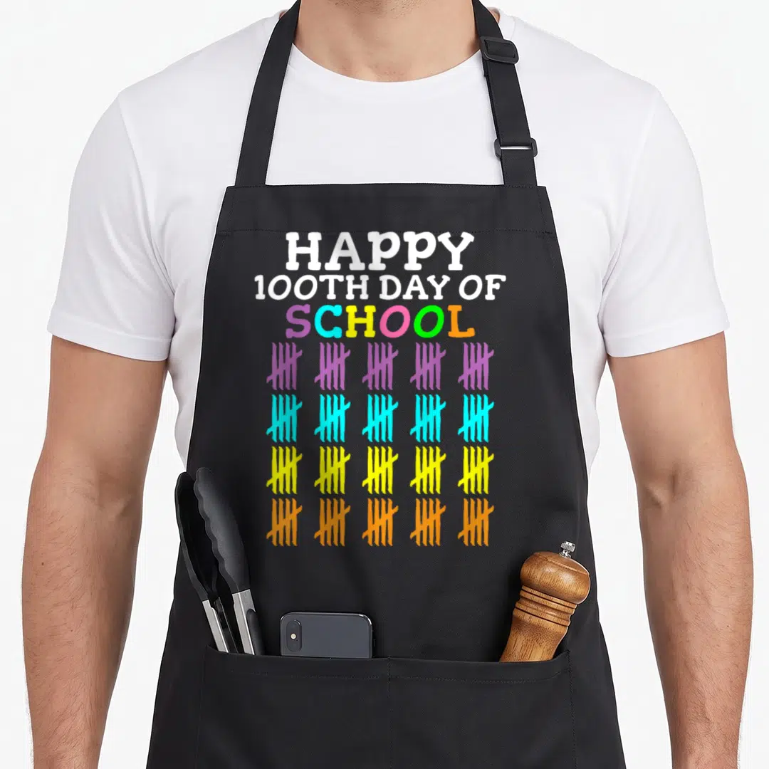 Cute school teacher apron - HAPPY 100TH DAY OF SCHOOL text above four rows of five colorful tally marks — shown on a black cotton canvas apron against a white background