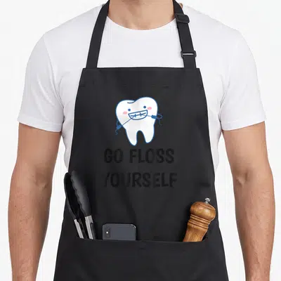 Yourself dentist apron - Cartoon tooth flossing self with GO FLOSS YOURSELF text below — shown on a black cotton canvas apron against a white background