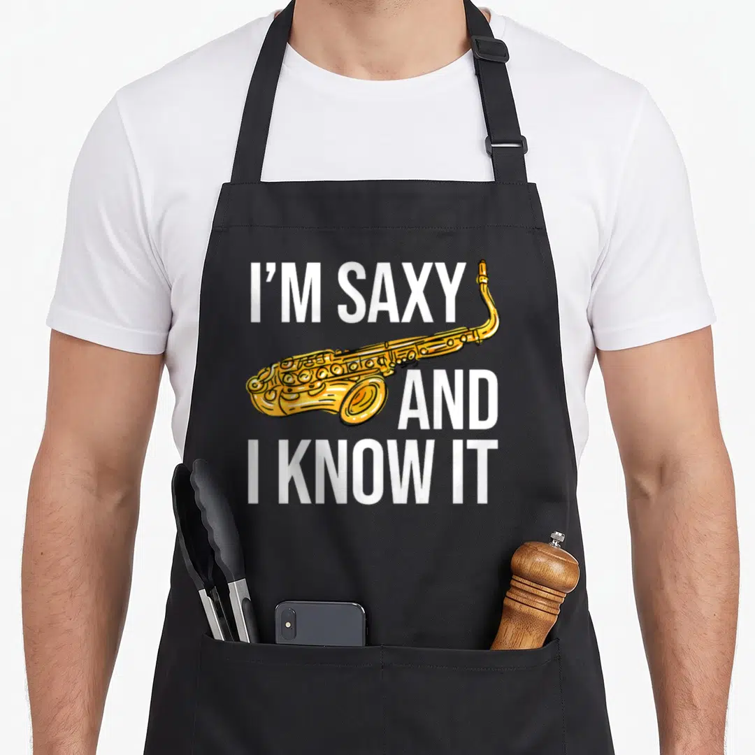 Saxophone teacher apron - I'M SAXY text and gold cartoon saxophone on grey background — shown on a black cotton canvas apron against a white background