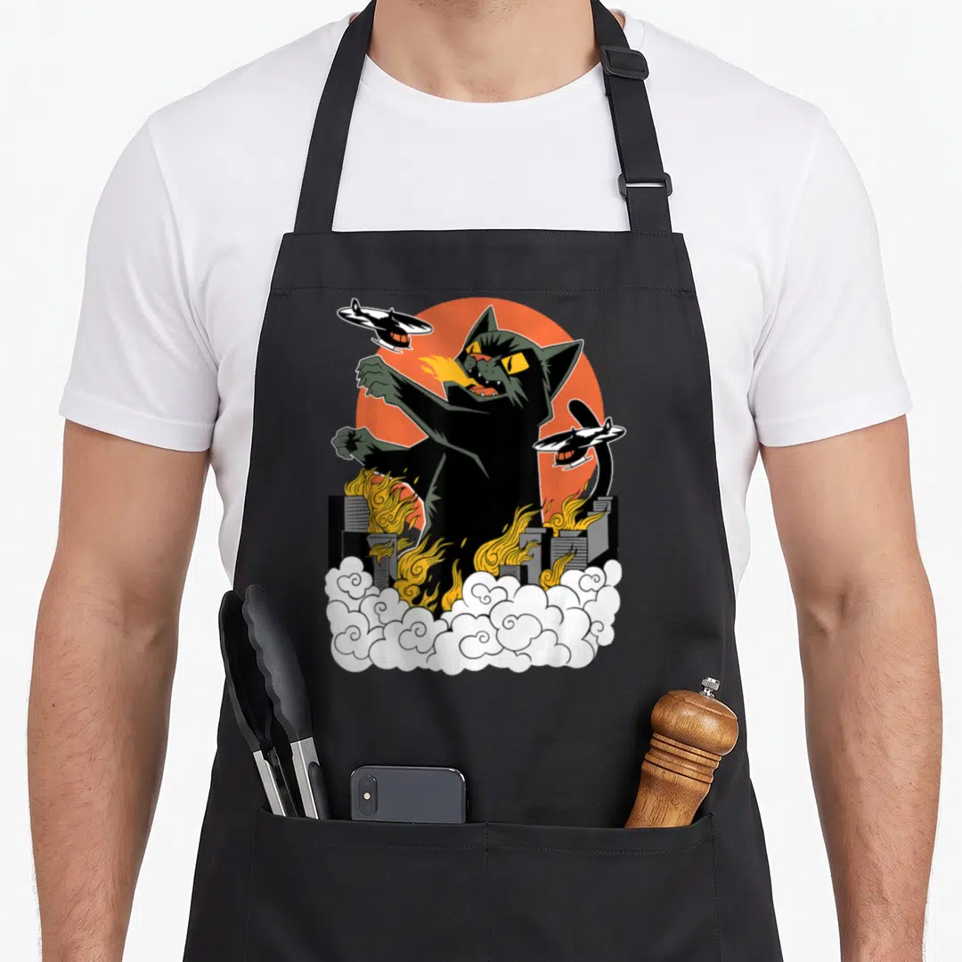 Japanese crew apron - Black cat breathing fire over city with helicopters and orange sun cartoon — shown on a black cotton canvas apron against a white background