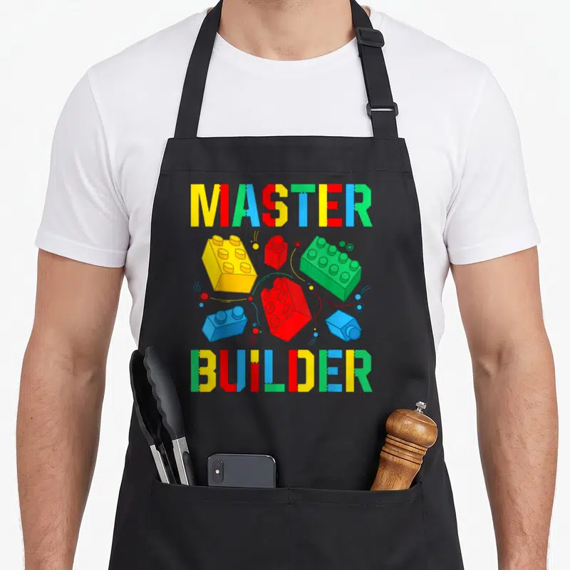 Toy block & apron - Master Builder text framing yellow red blue and green building blocks — shown on a black cotton canvas apron against a white background