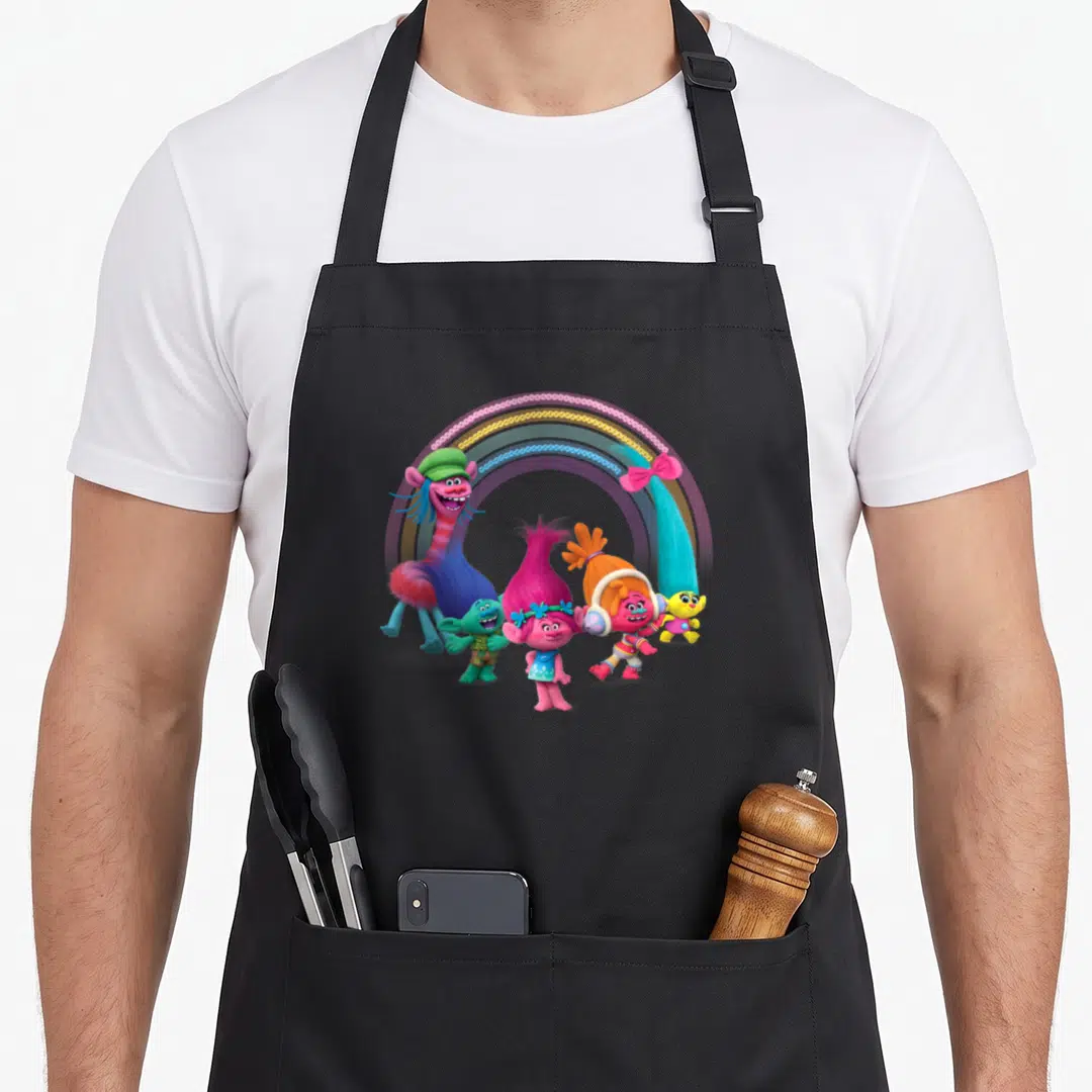 Troll rainbow apron - Five Trolls characters clustered under a rainbow arch in pink, blue, yellow, and orange — shown on a black cotton canvas apron against a white background