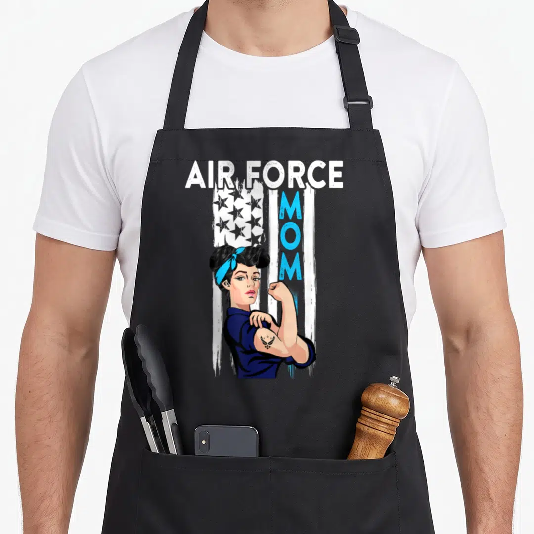 Costume air force mom apron - Cartoon woman flexing arm under AIR FORCE text with distressed flag and vertical MOM — shown on a black cotton canvas apron against a white background