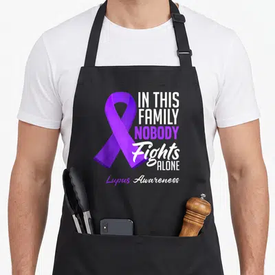 Lupus family aprons - Purple awareness ribbon next to IN THIS FAMILY NOBODY Fights ALONE text in white and purple — shown on a black cotton canvas apron against a white background