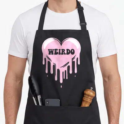 Dripping goth apron - Melting pink heart with grey WEIRDO text in cartoon style — shown on a black cotton canvas apron against a white background