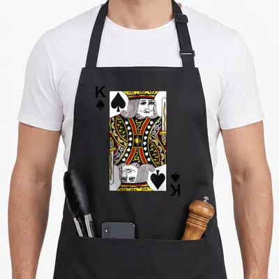 Poker king apron - Realistic King of Spades playing card with K and spade symbols in yellow, red, black, and white — shown on a black cotton canvas apron against a white background