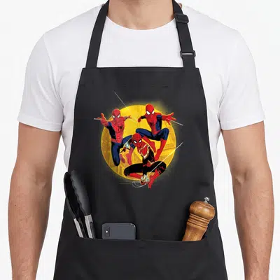 Way novelty apron - Three Spider-Men in red and blue suits posed before yellow circle with white web lines in cartoon — shown on a black cotton canvas apron against a white background