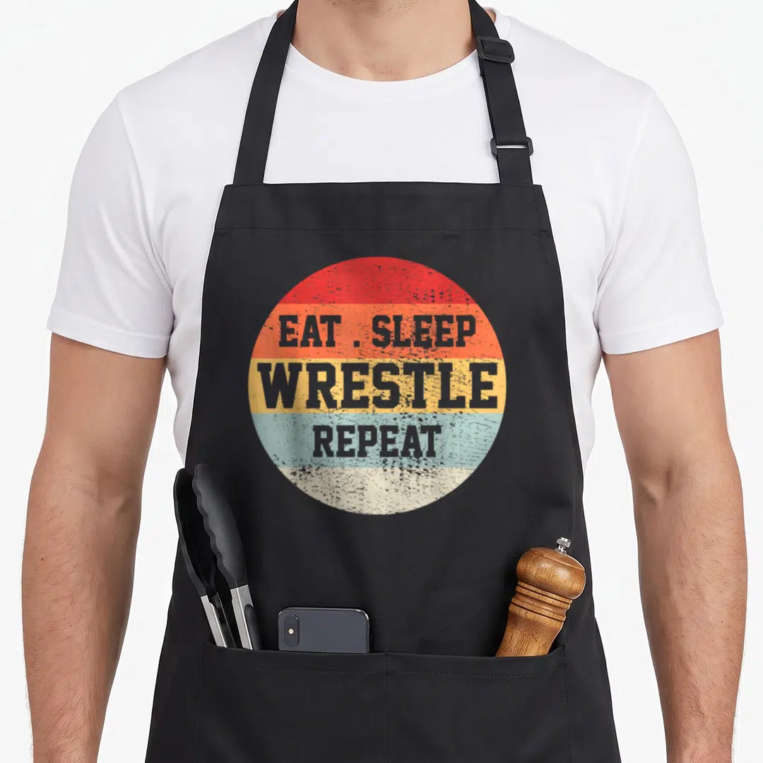 Funny wrestler wrestling apron - Retro circle with red orange yellow blue stripes and grey EAT SLEEP WRESTLE REPEAT text — shown on a black cotton canvas apron against a white background
