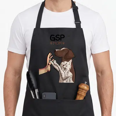Gsp german dog apron - Cartoon GSP dog high-fiving human hand with GSP MOM text and paw prints — shown on a black cotton canvas apron against a white background