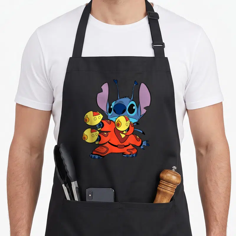 Space fighter apron - Blue cartoon character in orange suit holding yellow spheres with purple ears standing — shown on a black cotton canvas apron against a white background