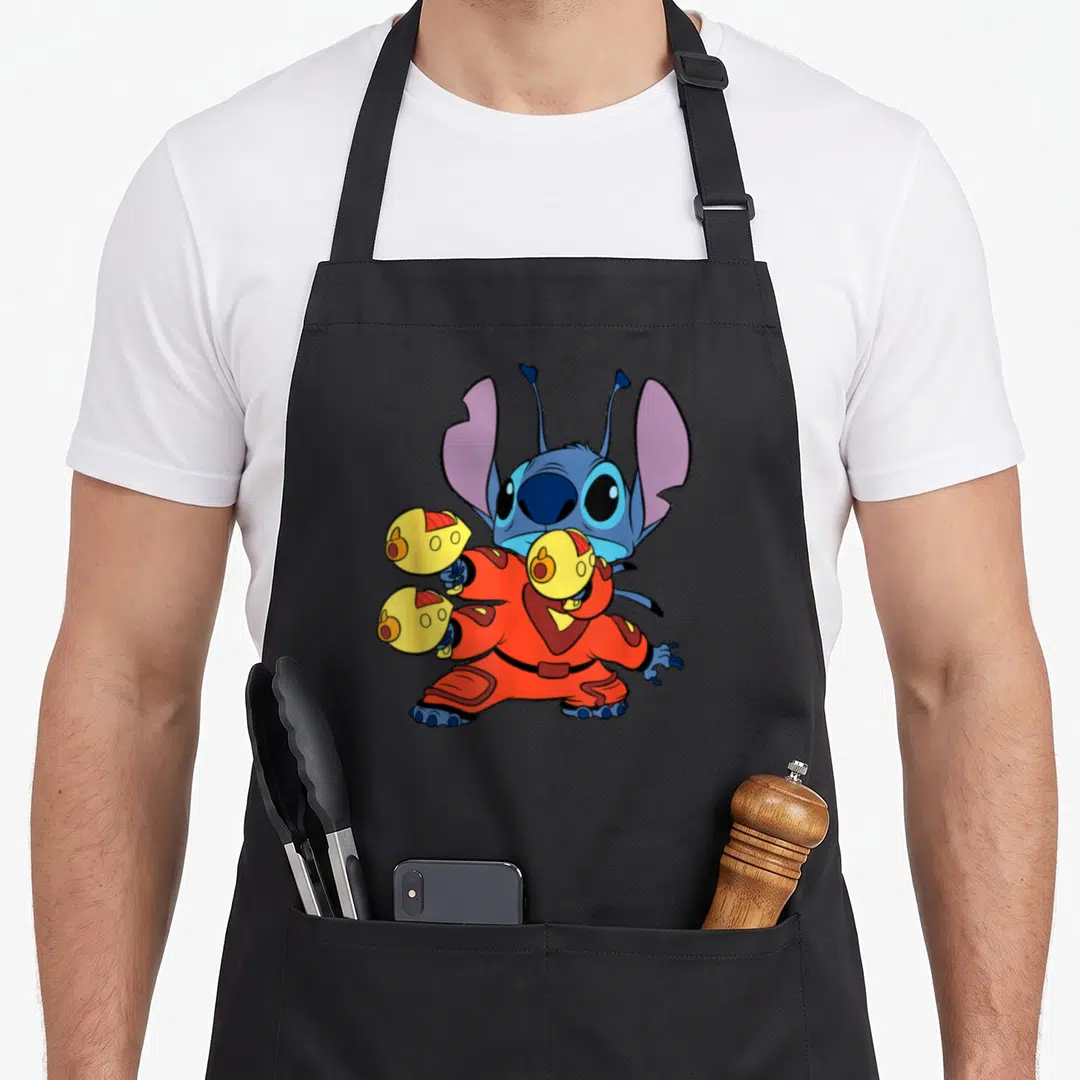 Space fighter apron - Blue cartoon character in orange suit holding yellow spheres with purple ears standing — shown on a black cotton canvas apron against a white background