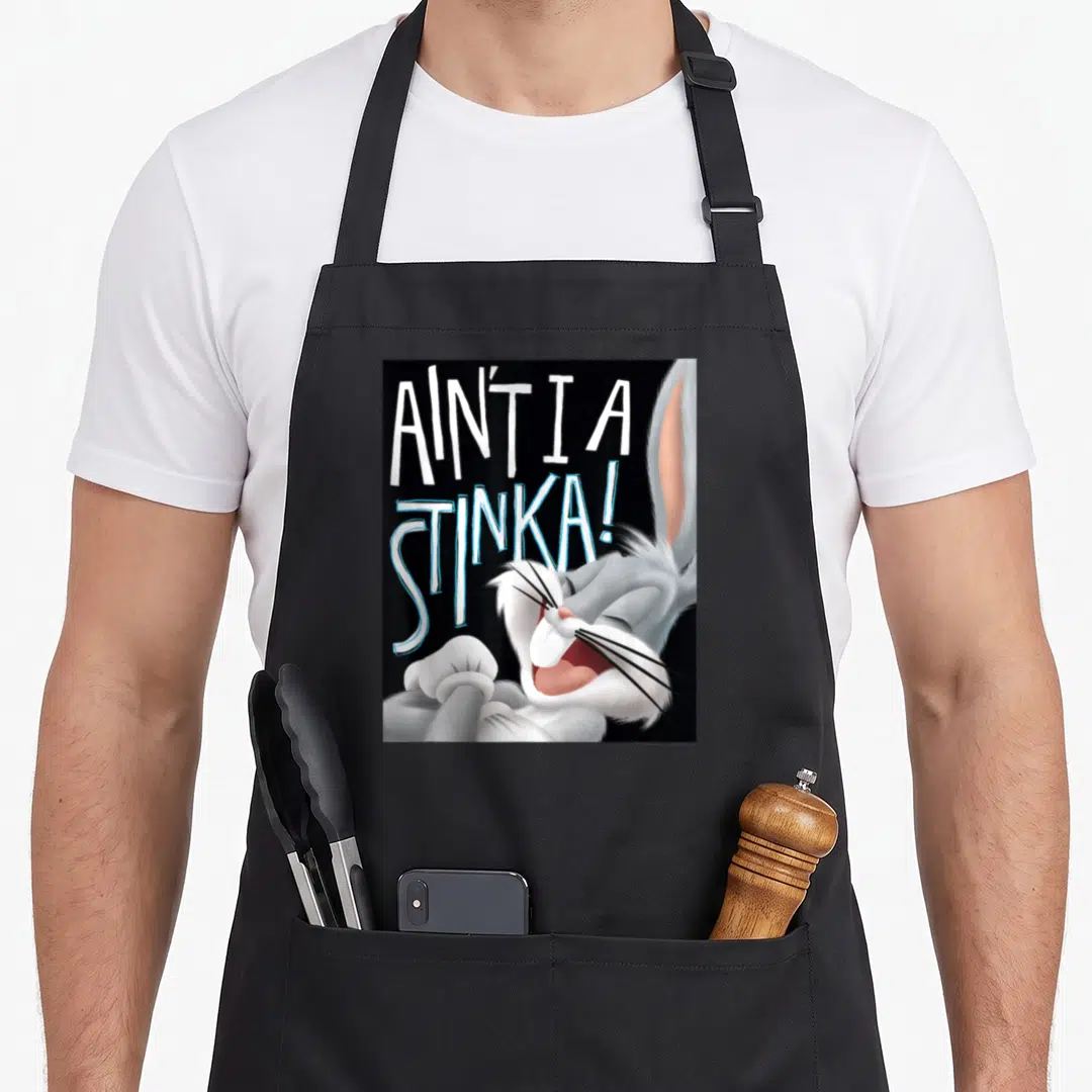 Stinka bunny apron - Bugs Bunny laughing next to AIN'T I A STINKA! text in white and blue — shown on a black cotton canvas apron against a white background