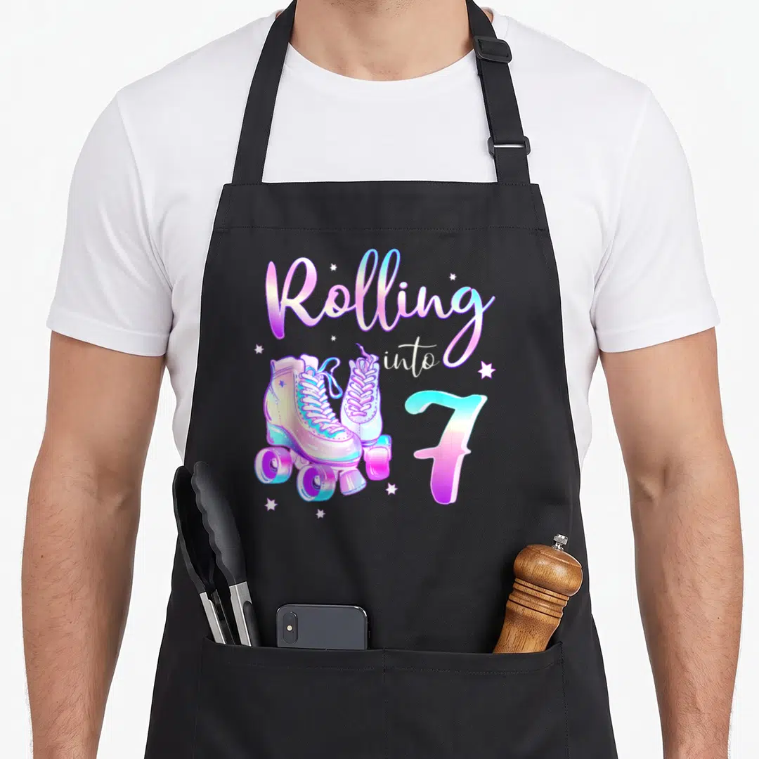 7th bday birthday apron - Rolling into 7 text with pink blue roller skates and stars — shown on a black cotton canvas apron against a white background