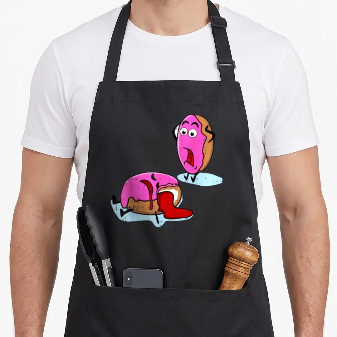 Dead donut apron - Two cartoon donuts, one standing shocked, one lying in red puddle, pink and brown — shown on a black cotton canvas apron against a white background