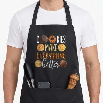 Better women's christmas aprons - Stacked text reading Cookies Make Everything Better with cartoon cookies replacing — shown on a black cotton canvas apron against a white background