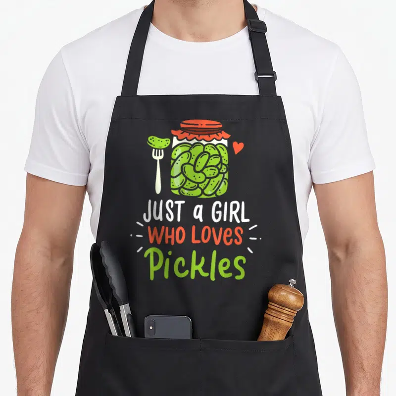 Cucumber canning apron - Cartoon pickle jar, fork, heart, and text JUST a GIRL WHO LOVES Pickles — shown on a black cotton canvas apron against a white background