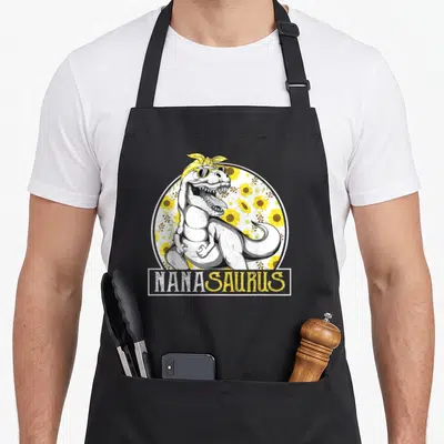 Sunflower nana aprons - Cartoon T-Rex with sunglasses and yellow headband in front of sunflowers with NANASAURUS text — shown on a black cotton canvas apron against a white background