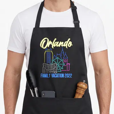 Orlando family aprons - Neon line art of Orlando skyline with FAMILY VACATION 2022 text — shown on a black cotton canvas apron against a white background