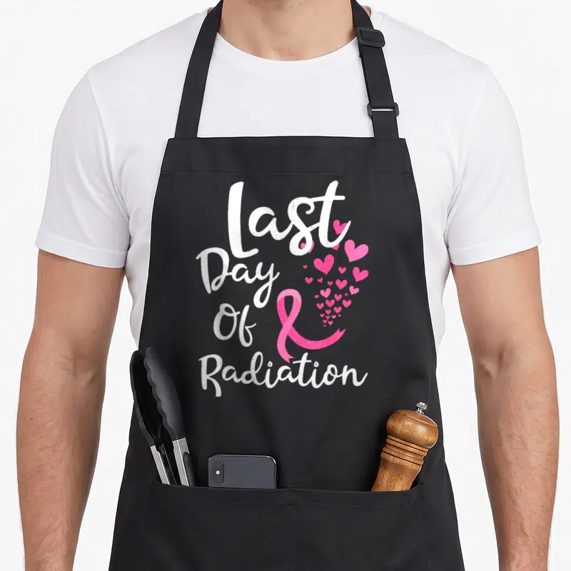Breast radiation aprons - Last Day Of Radiation text with pink ribbon and heart cluster — shown on a black cotton canvas apron against a white background