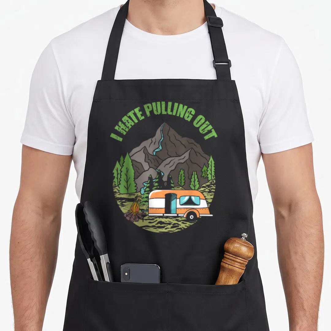 Camping travel trailer apron - I HATE PULLING OUT text over cartoon camper, mountains, trees and campfire — shown on a black cotton canvas apron against a white background