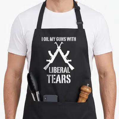 Oil 2nd apron - Two crossed white rifles with distressed text reading I OIL MY GUNS WITH LIBERAL TEARS — shown on a black cotton canvas apron against a white background