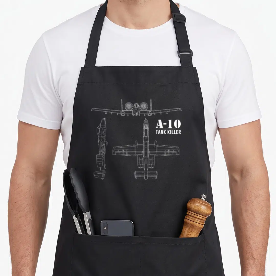 Killer warthog apron - White line drawings of A-10 aircraft front side and top views with A-10 Tank Killer text — shown on a black cotton canvas apron against a white background