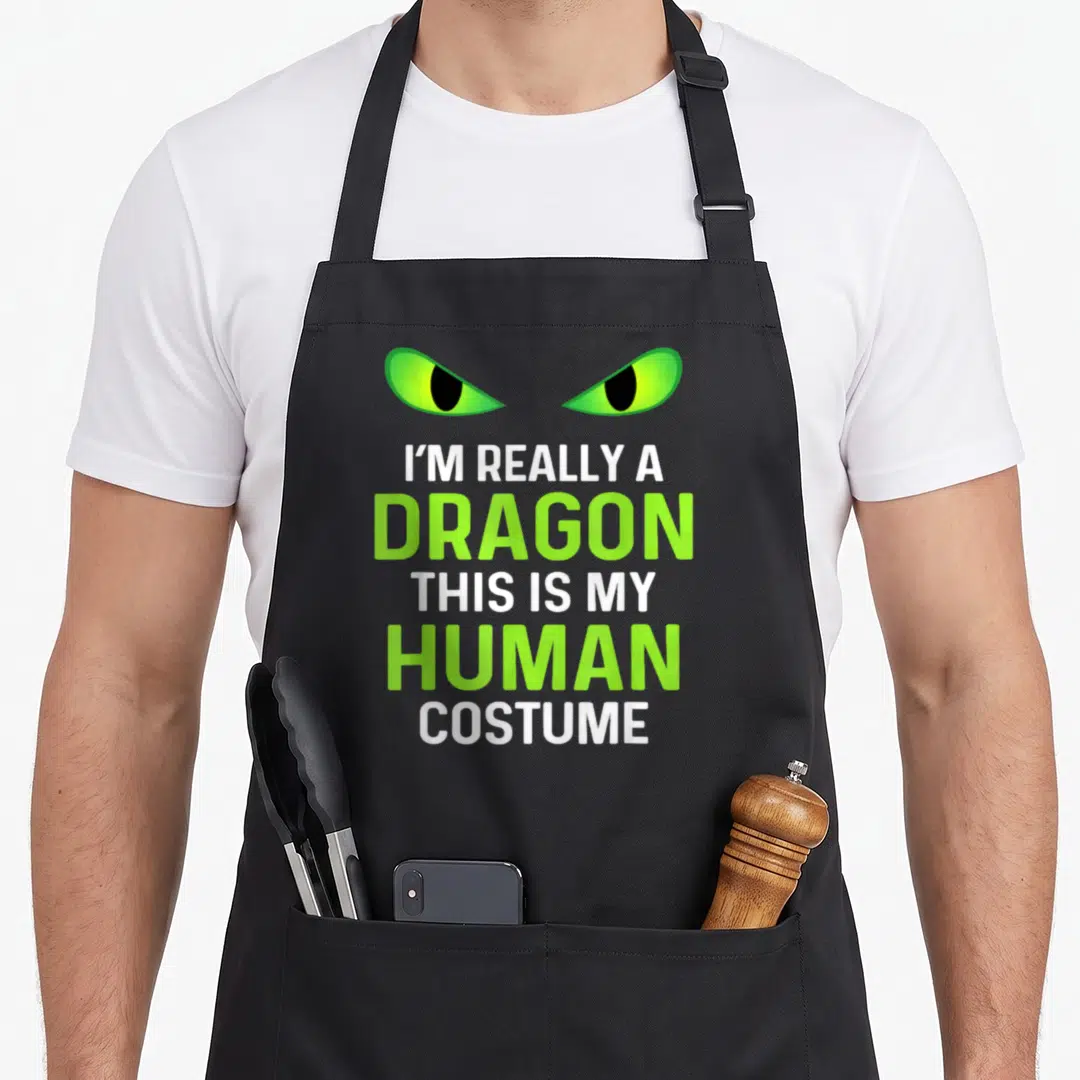 Costume dragon apron - Two green dragon eyes above stacked white and green text declaring the wearer is actually — shown on a black cotton canvas apron against a white background