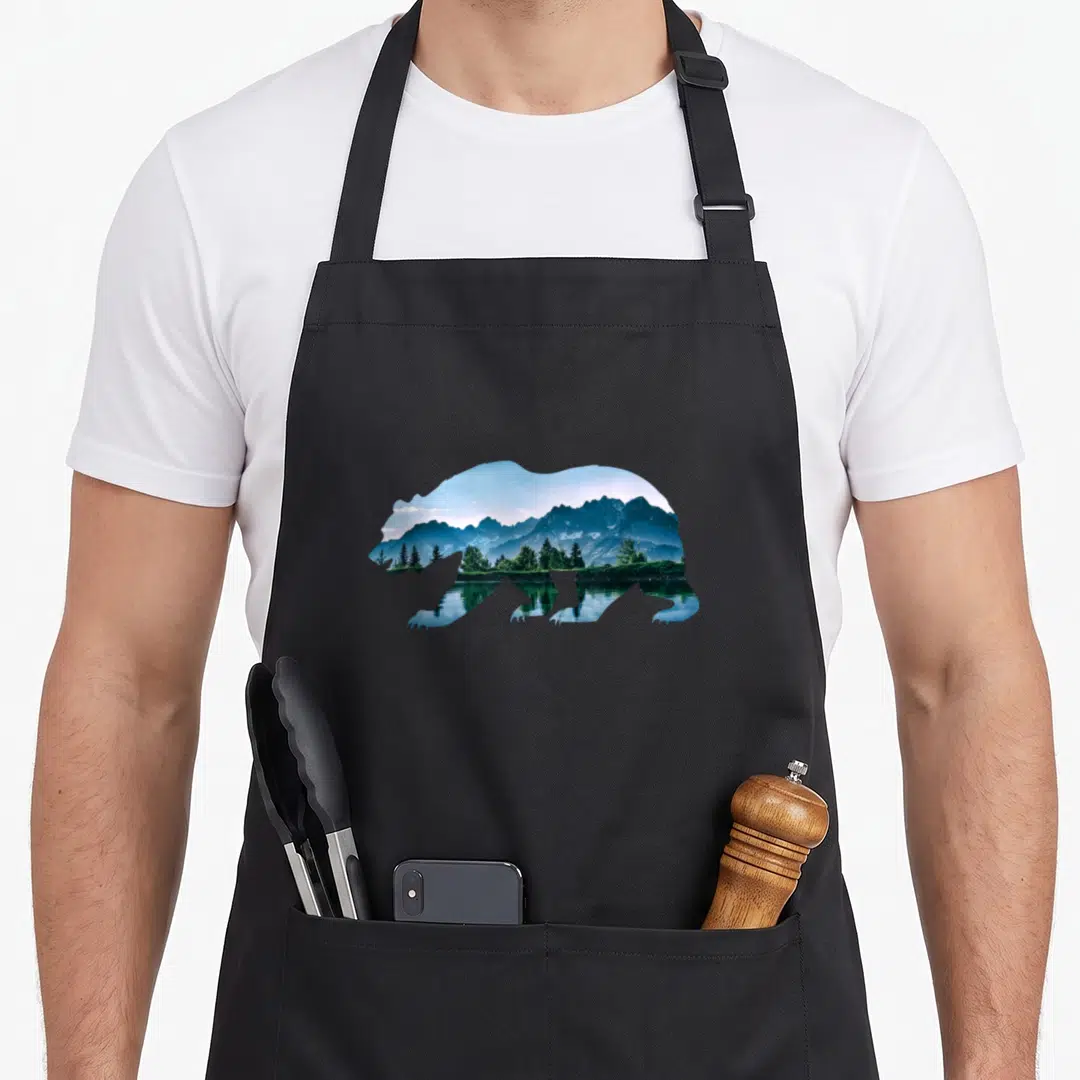 Wildlife bear apron - Bear silhouette containing blue mountains, green trees, and lake reflection photo — shown on a black cotton canvas apron against a white background