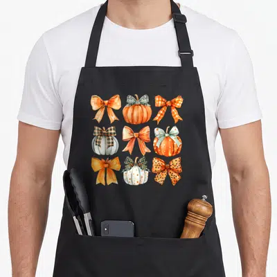 Bow thanksgiving apron - Watercolor grid of orange and teal bows and pumpkins with polka dots and plaid patterns — shown on a black cotton canvas apron against a white background