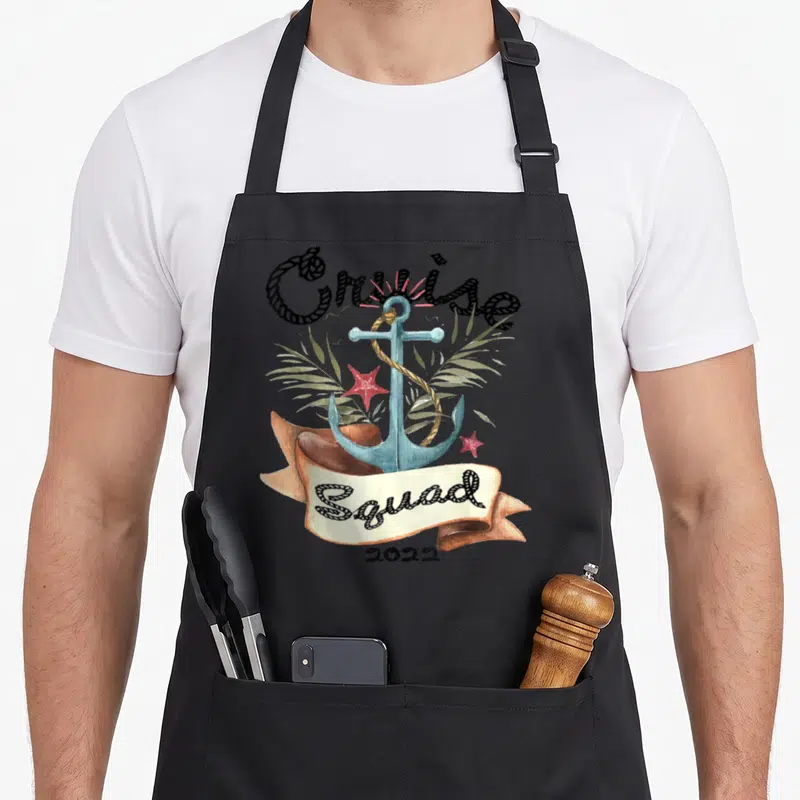 Cruise holiday apron - Watercolor blue anchor, tan banner with Squad text, red starfish, and green palm leaves — shown on a black cotton canvas apron against a white background