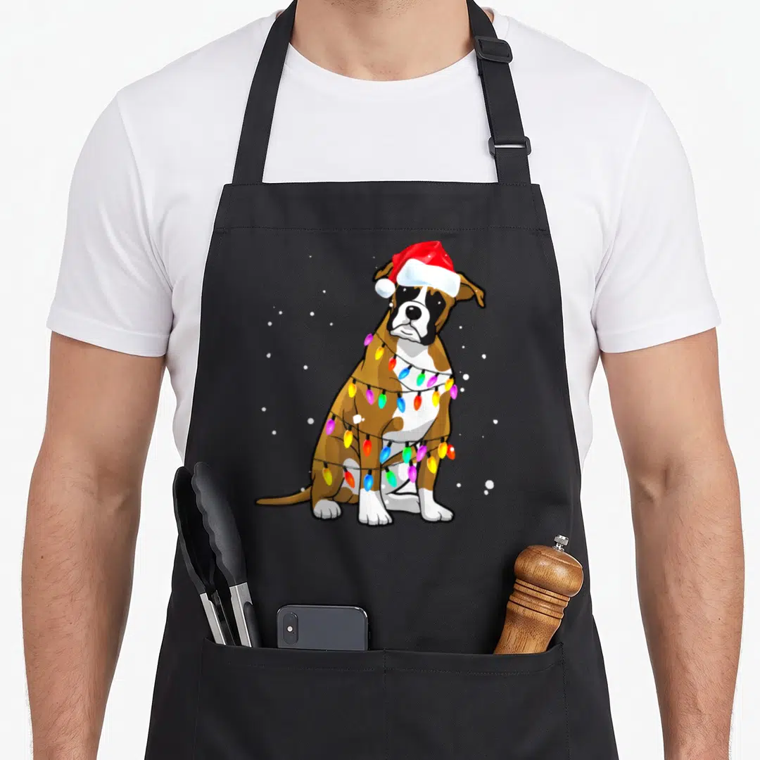 Christmas boxer dog apron - Cartoon boxer dog in red santa hat wrapped in multicolored Christmas lights with snowflakes — shown on a black cotton canvas apron against a white background