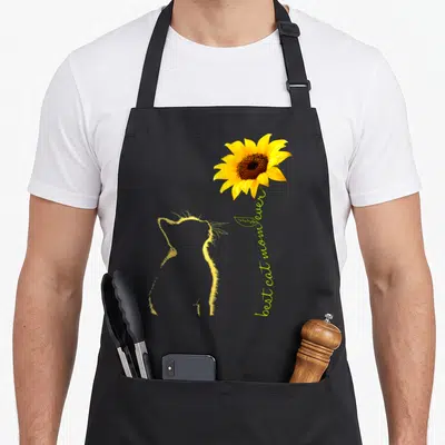 Sunflower cat in an apron - Yellow cat outline next to sunflower with vertical best cat mom ever text — shown on a black cotton canvas apron against a white background
