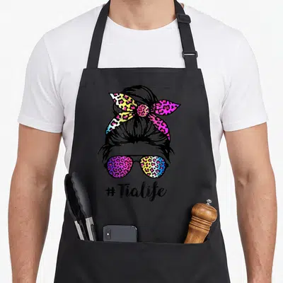 Tia leopard aprons - Rainbow leopard pattern on sunglasses and bun with # Tialife text below — shown on a black cotton canvas apron against a white background