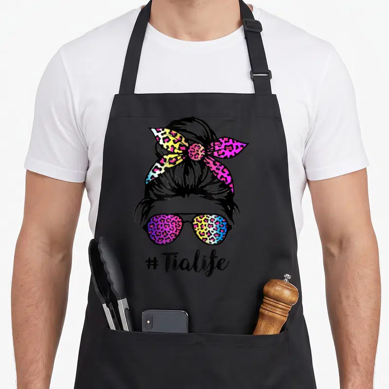 Tia leopard aprons - Rainbow leopard pattern on sunglasses and bun with # Tialife text below — shown on a black cotton canvas apron against a white background