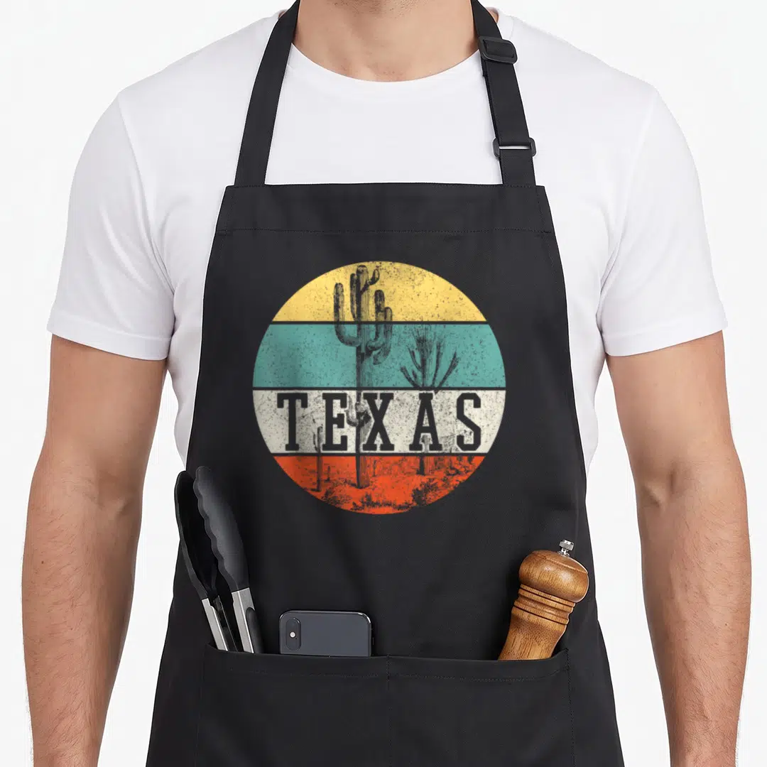 Texas country apron - Retro cactus graphic over yellow teal white and orange bands with TEXAS text in grey — shown on a black cotton canvas apron against a white background
