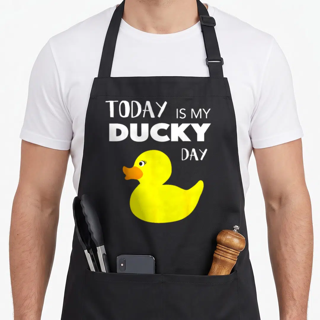 Today rubber apron - Yellow cartoon duck with orange beak and white TODAY IS MY DUCKY DAY text — shown on a black cotton canvas apron against a white background