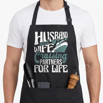 Cruiser husband wife aprons - White and teal typography with a cruise ship and five hearts above the lettering — shown on a black cotton canvas apron against a white background
