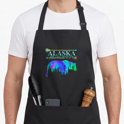 Light bear apron - Alaska text between arrows above multicolored bear silhouette containing forest scene — shown on a black cotton canvas apron against a white background