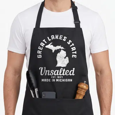 Michigan lake pride apron - White distressed Michigan map with Great Lakes State and Unsalted text — shown on a black cotton canvas apron against a white background