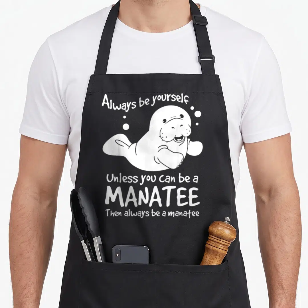 Alway manatee lover apron - White cartoon manatee surrounded by bubbles and text about being a manatee — shown on a black cotton canvas apron against a white background