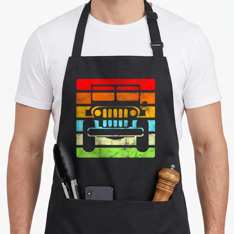 70s road apron - Grey jeep silhouette over five colored stripes red orange yellow blue green — shown on a black cotton canvas apron against a white background