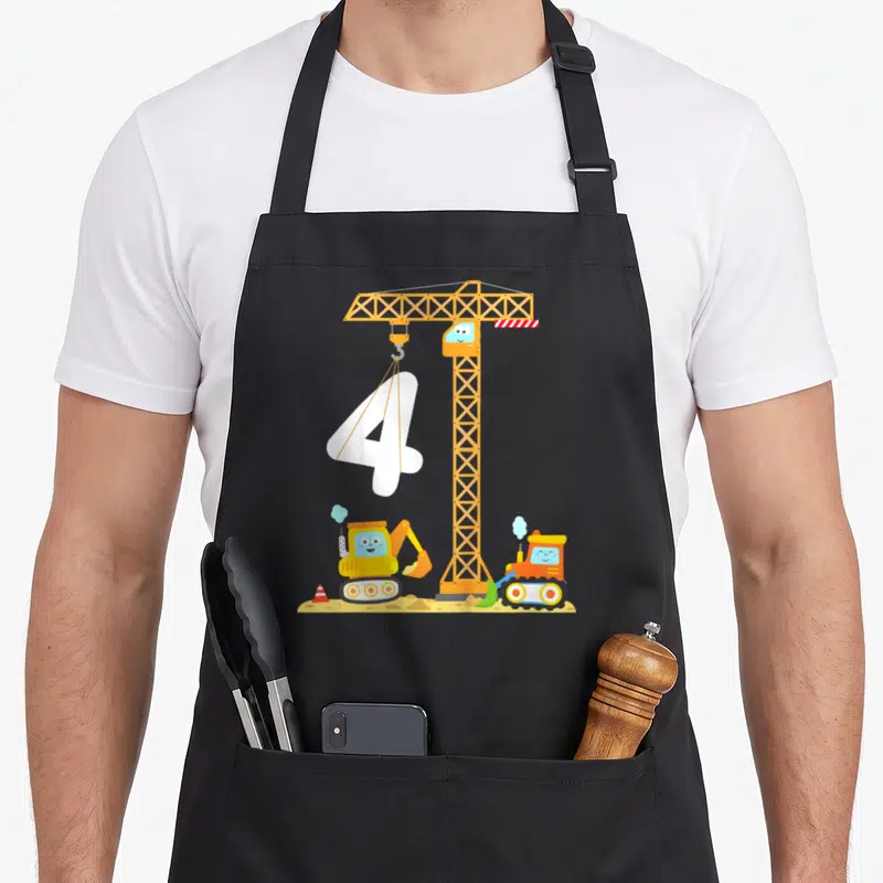 Digger vehicle apron - Cartoon crane lifting white number 4 above excavator and bulldozer on dirt — shown on a black cotton canvas apron against a white background