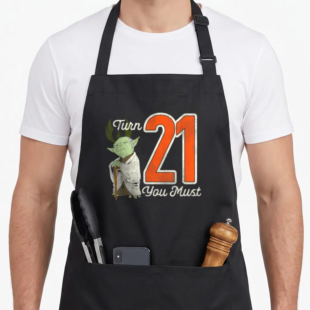 Yoda 21st birthday apron - Cartoon Yoda standing beside orange number 21 with white text Turn You Must — shown on a black cotton canvas apron against a white background