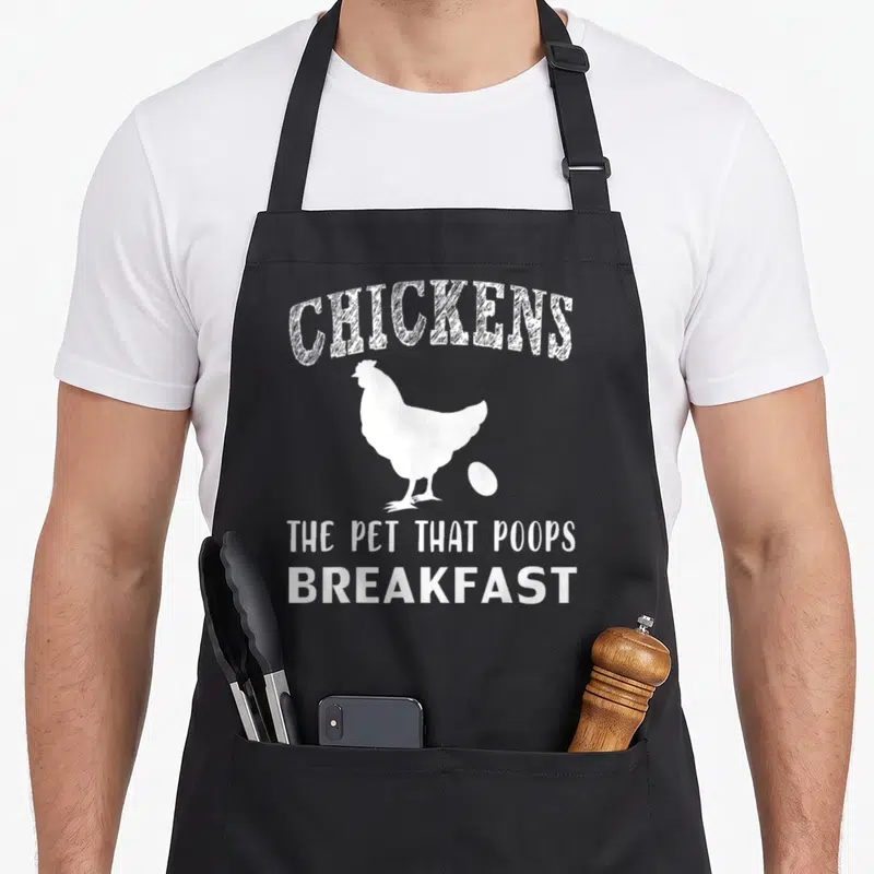 Pet chicken apron - White arched text CHICKENS above chicken silhouette and egg with stacked text below — shown on a black cotton canvas apron against a white background