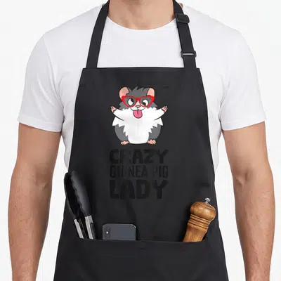 Cool guinea pet apron - Cartoon guinea pig with red glasses above stacked text CRAZY GUINEA PIG LADY — shown on a black cotton canvas apron against a white background