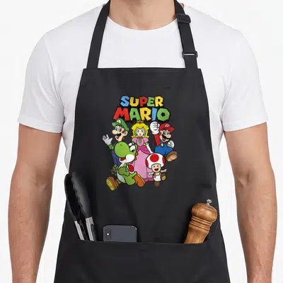 Funny heroe apron - SUPER MARIO text above five cartoon characters in red blue yellow green and pink — shown on a black cotton canvas apron against a white background