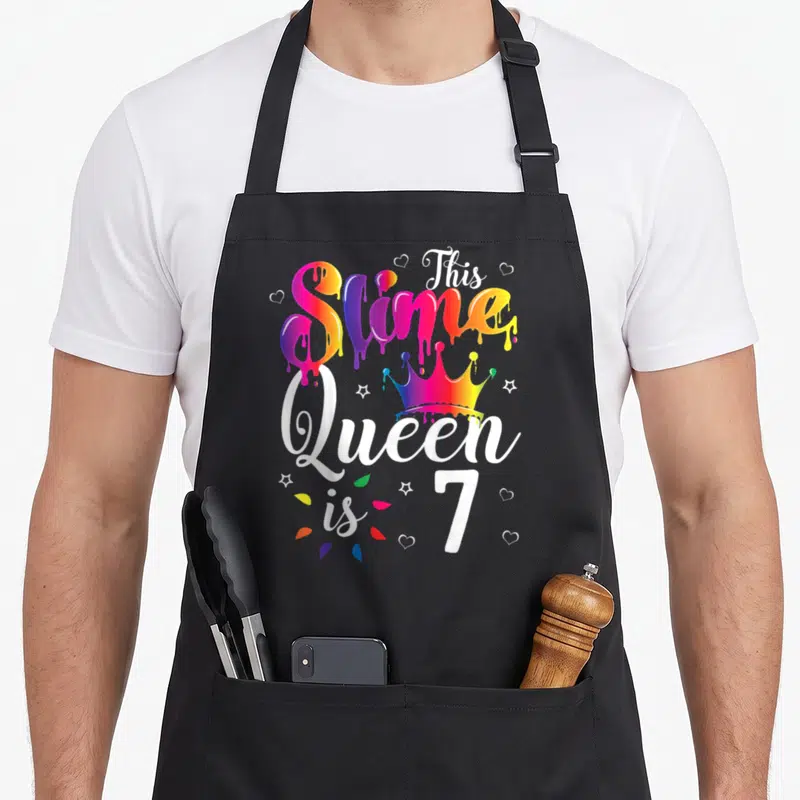 7th queen of baking apron - This Slime Queen is 7 rainbow dripping text with crown and hearts — shown on a black cotton canvas apron against a white background