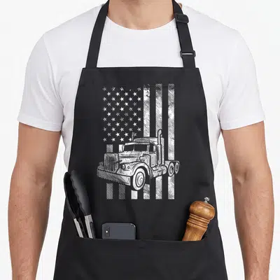 Trucking american flag apron - White line art of a semi-truck positioned in front of a distressed American flag pattern — shown on a black cotton canvas apron against a white background